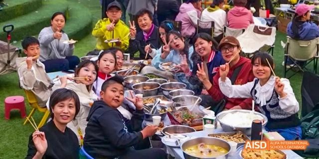 Camford Royal School students and teachers gathered around a large shared meal, smiling and posing.