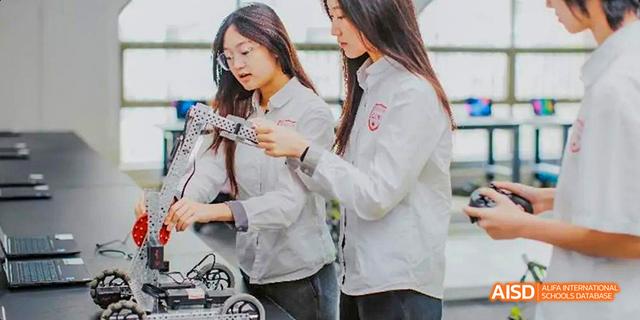 Two female students from the Canadian International School of Guangzhou are collaborating on a project while holding a small robotic device.