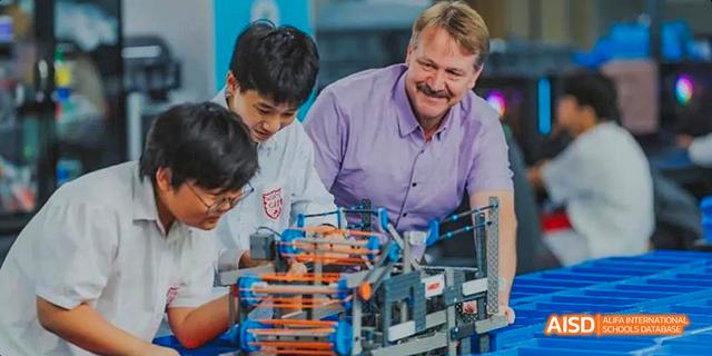 A teacher from the Canadian International School of Guangzhou smiles while working with two students on a hands-on project.