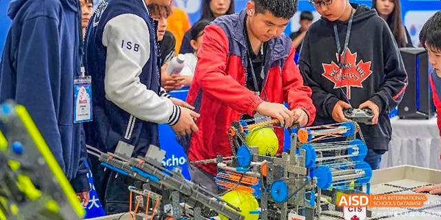 A group of students from the Canadian International School of Guangzhou is focused on a robotic device with yellow components.