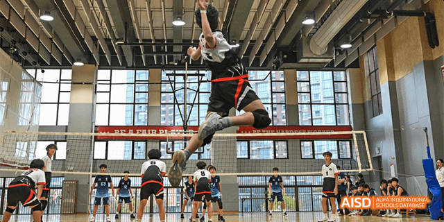 A student from the Canadian International School of Guangzhou is mid-air, attempting to spike a volleyball during a game.