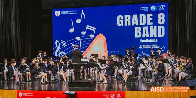 An orchestra from the Canadian International School of Guangzhou performs on a stage, with the conductor facing the audience.