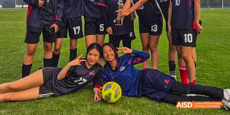 Two female students from the Canadian International School of Guangzhou pose together on a grass field, one resting next to a volleyball.