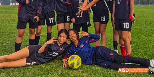 Two female students from the Canadian International School of Guangzhou pose together on a grass field, one resting next to a volleyball.