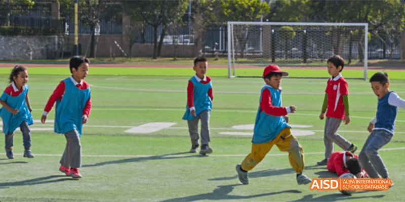 A young student from the Canadian International School of Guangzhou in a red and blue outfit is playing outside on a grassy field.