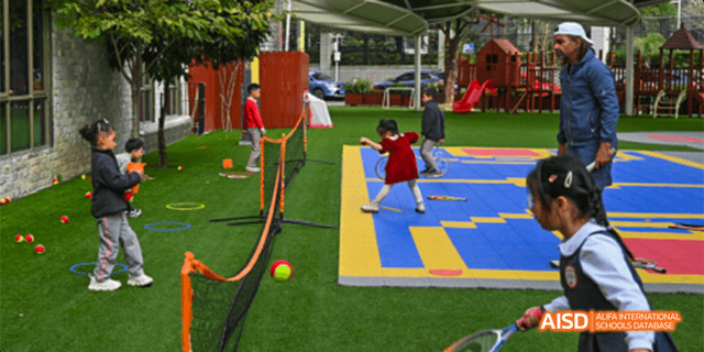 A student from the Canadian International School of Guangzhou is playing a game, throwing a yellow ball at a goal on a blue and yellow mat.