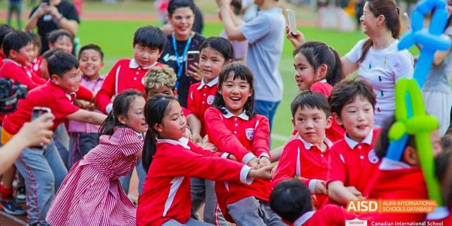 A group of students from the Canadian International School of Guangzhou participates in a tug-of-war game, all wearing red shirts.