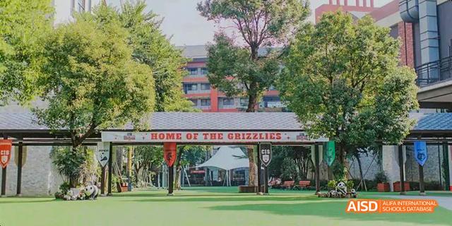 A sign reading "Home of the Grizzlies" stands in front of the Canadian International School of Guangzhou campus, with a red archway in the background.