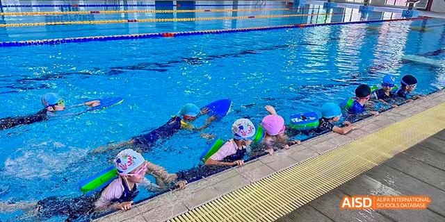 A group of students from the Canadian International School of Guangzhou are in a swimming pool, with one wearing a pink swim cap.
