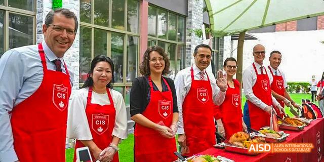 A group of staff members from the Canadian International School of Guangzhou, all wearing red aprons, stand together.