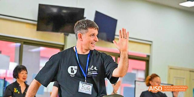 A male staff member from the Canadian International School of Guangzhou with a big smile waves to the camera.