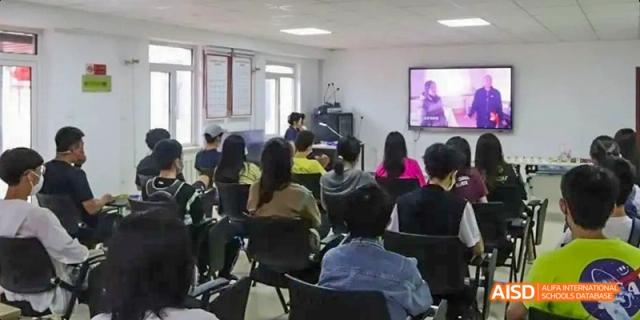 A group of people at Dalian American International School listening to a speaker in a classroom.