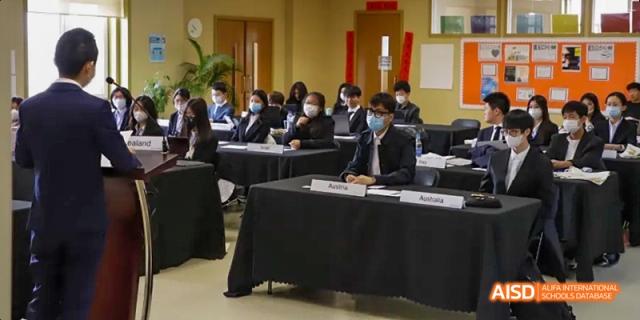Students dressed in suits and ties at Dalian American International School sitting at tables in a conference room.