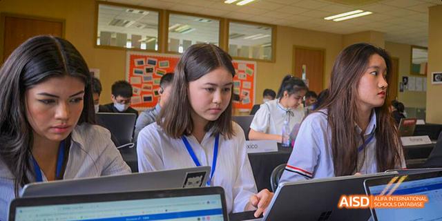 A young person at Dalian American International School with a badge on sitting at a desk and using a laptop.