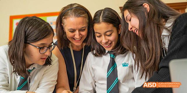 A teacher at Dalian American International School smiling at a student who is wearing a school tie.