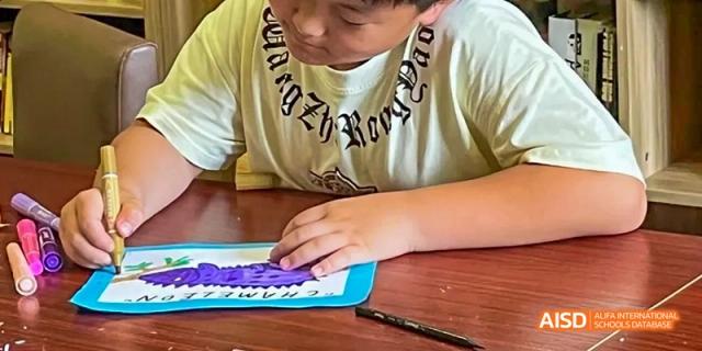A young person at Dalian American International School drawing or writing on a paper.