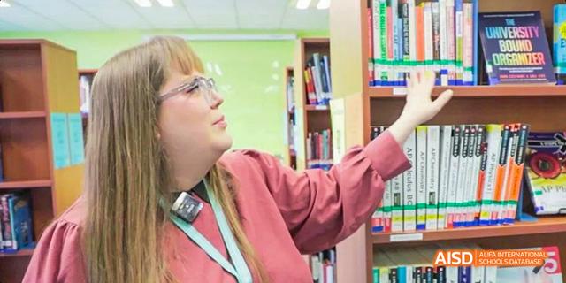 A young person at Dalian American International School reaching for a book on a shelf in a library.