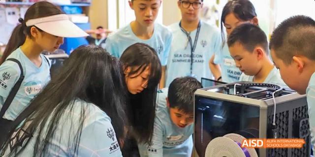 A group of students at Dalian American International School gathered around a desk and looking at something together.