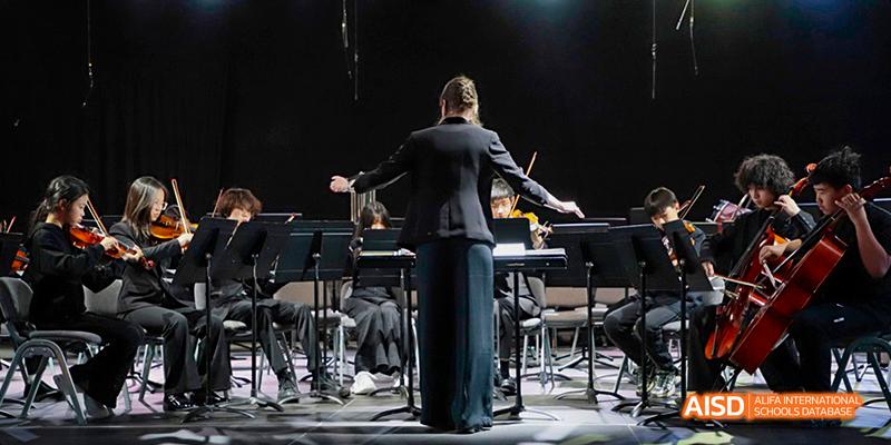 A conductor is leading an orchestra on a stage at Dalian American International School.
