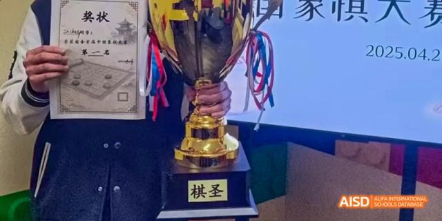 A person is holding a gold trophy with ribbons, at an event for Dalian American International School.