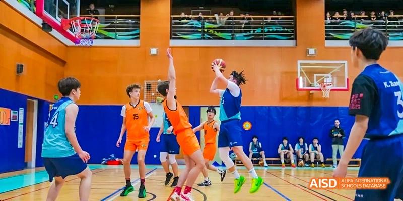 Two male students from Dalian American International School are playing basketball in a gymnasium.