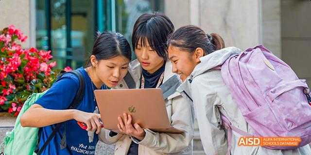 Two students and a teacher looking at a laptop together at Dalian American International School.