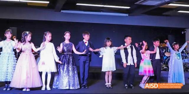 Two young children performing on a stage with a man and woman behind them, all dressed formally at Dalian American International School.