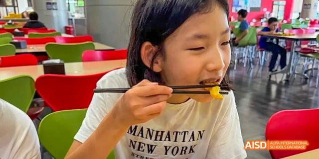 A young person eating with chopsticks at Dalian American International School.
