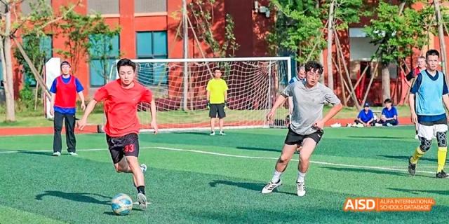 Dipont KCS Chengdu students play a game of soccer on a green field.