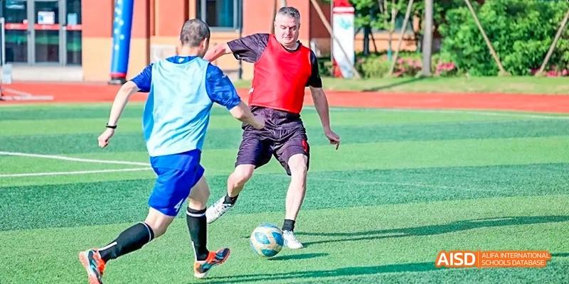 Two Dipont KCS Chengdu students in red and blue uniforms compete for the ball during a soccer game.