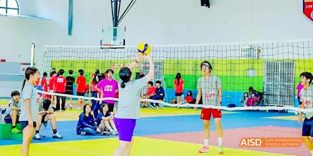Dipont KCS Chengdu students play a game of volleyball in a gymnasium.