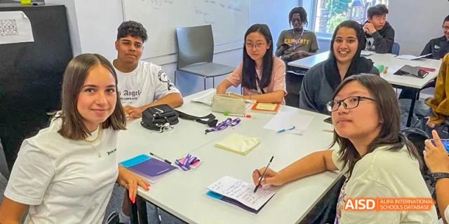 A group of Ealing International School students are working at a table, taking notes and using a laptop.