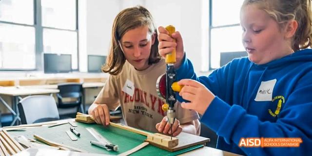 A young female Ealing International School student is using a tool to work on a small wooden project.