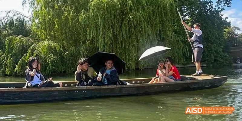 Ealing International School students are punting in a boat on a river, with green trees hanging over the water.