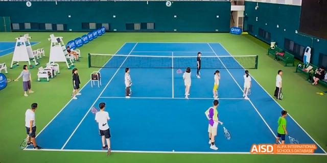 Ealing International School students playing tennis on a blue tennis court.