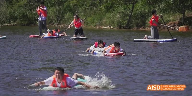 Ealing International School students participating in a water activity, with one person on a surfboard being pulled by others.