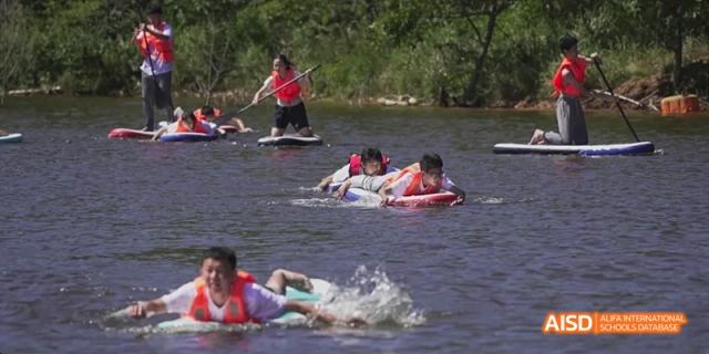 Ealing International School students participating in a water activity, with one person on a surfboard being pulled by others.