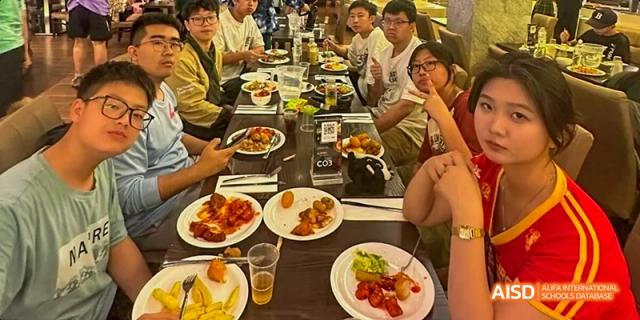 Ealing International School students are sitting together at a long table, eating a meal.