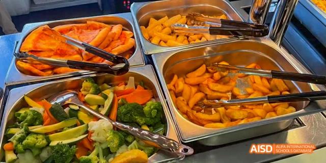 A close-up of a buffet at Ealing International School with a variety of hot dishes, including vegetables and potatoes.
