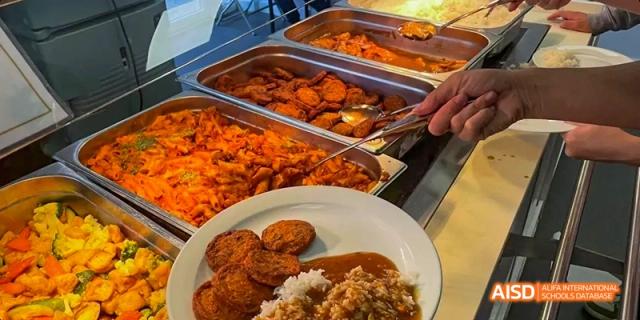 A plate of food is being prepared at Ealing International School's cafeteria, showing what appears to be fried food with gravy and rice.