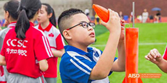A student wearing a blue shirt and glasses, holding an orange object and looking up at an event at Fuzhou Concord College of Sino-Canada.