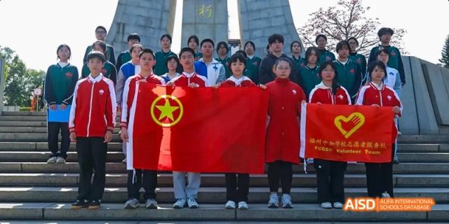 A group of students holding a red flag with a yellow star in front of a stone monument at Fuzhou Concord College of Sino-Canada.