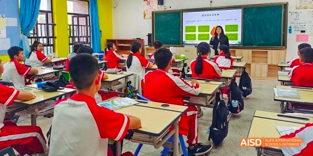A classroom scene with students in red and white uniforms seated at desks and looking at a large digital screen during a lesson at Fuzhou Concord College of Sino-Canada.