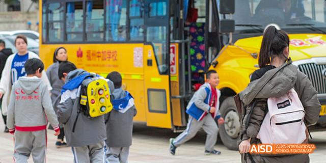 Students running to board a school bus with Chinese characters on the side at Fuzhou Concord College of Sino-Canada.