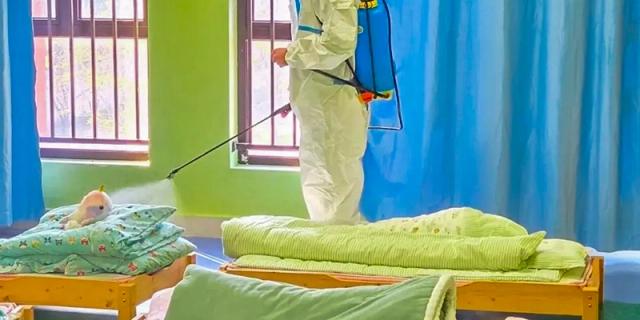 Fuzhou Concord College of Sino-Canada - A person wearing a white hazmat suit is spraying disinfectant in a room with a bed.