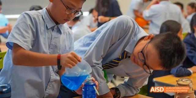 A close-up shot of a student from HAIDE Bilingual School Dongguan pouring a blue liquid from a beaker during a science experiment.