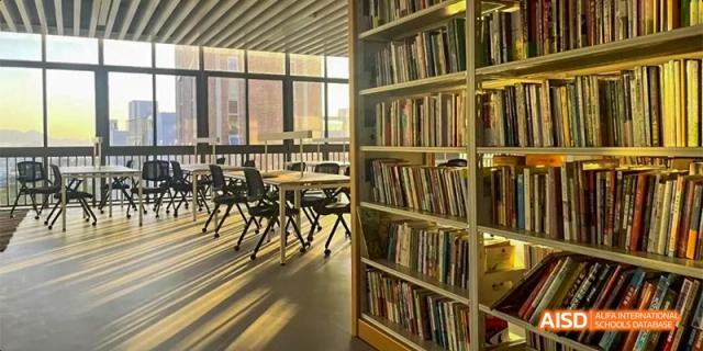 An empty library at HAIDE Bilingual School Dongguan with bookshelves full of books and tables and chairs in the background.