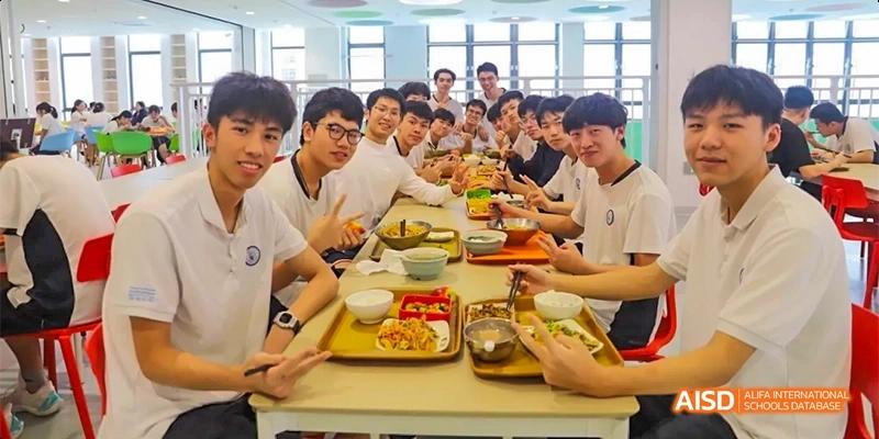 A group of students from HAIDE Bilingual School Dongguan sitting at tables and enjoying a meal together in the school cafeteria.