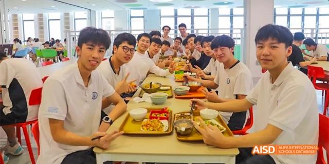 A group of students from HAIDE Bilingual School Dongguan sitting at tables and enjoying a meal together in the school cafeteria.
