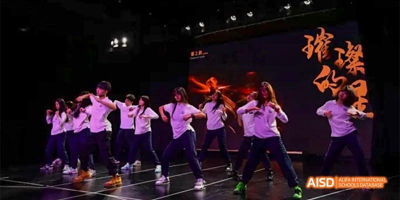 A group of students from HAIDE Bilingual School Dongguan performing a dance routine on a stage with purple lighting.